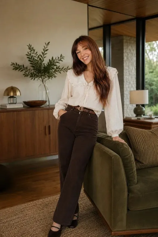 Jewel standing beside an olive velvet sofa in a wood-paneled room.